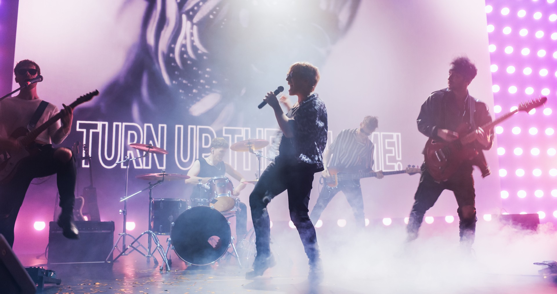 Rock Musicians in Fashionable Outfits Performing Alternative Punk Rock Music on a Nightclub Stage. Focus on a Beautiful Female Drummer Playing Drums Under Bright Spotlights, Bringing Energy to Fans